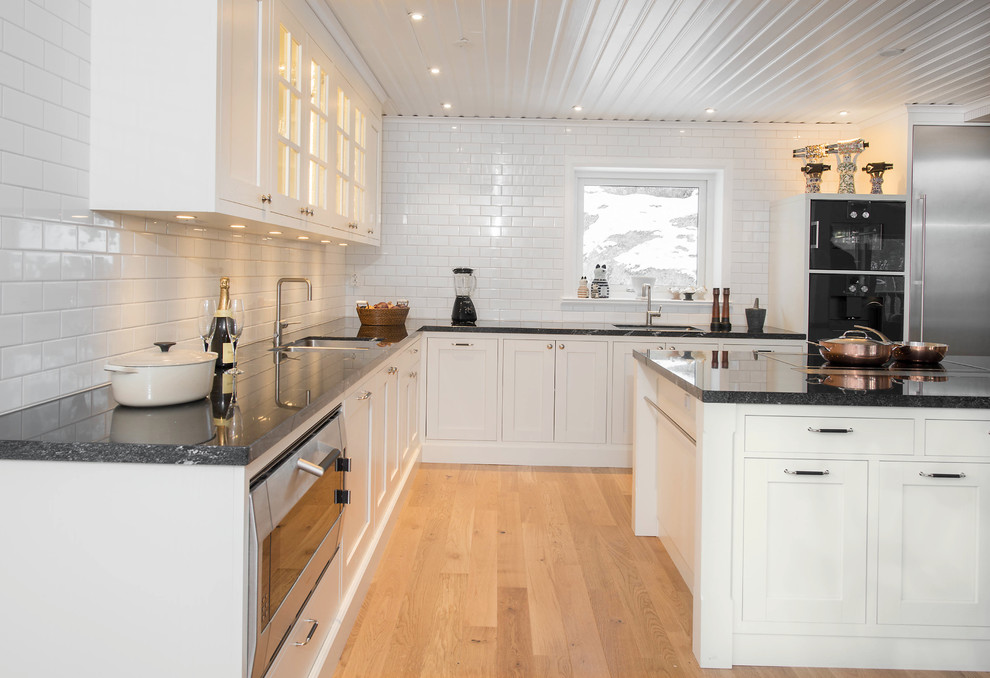 Photo of a classic l-shaped kitchen/diner in Stockholm with a submerged sink, shaker cabinets, white cabinets, granite worktops, white splashback, porcelain splashback and stainless steel appliances.