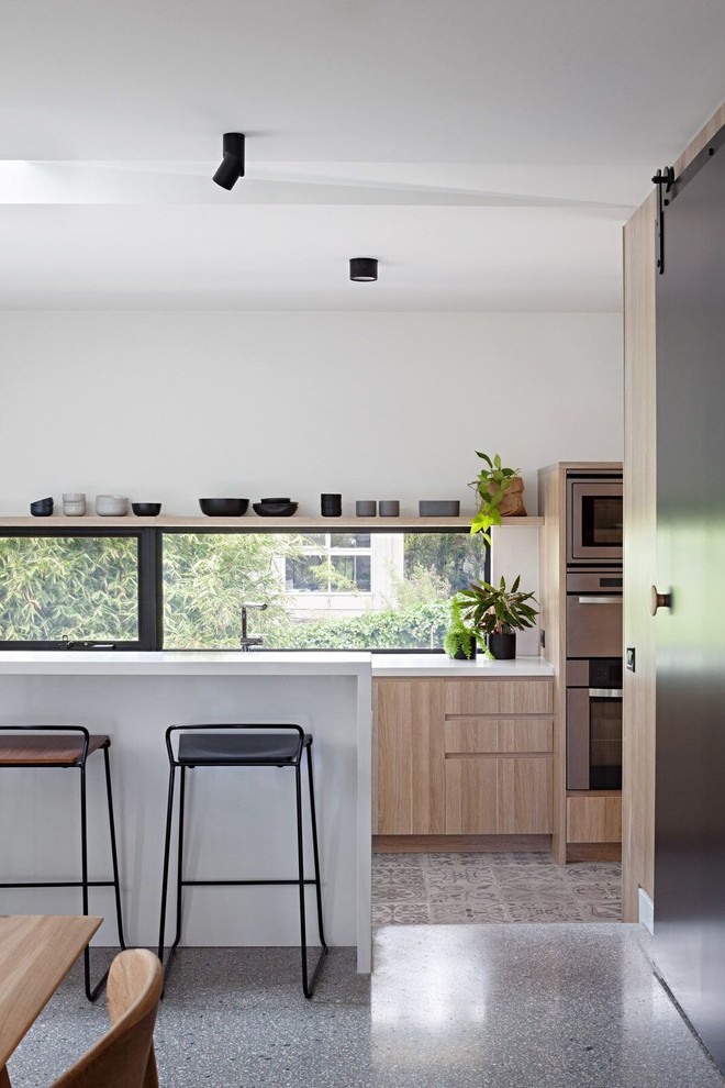 Esempio di un cucina con isola centrale minimal di medie dimensioni con ante in legno chiaro, top in quarzo composito, elettrodomestici in acciaio inossidabile, pavimento con piastrelle in ceramica e ante lisce
