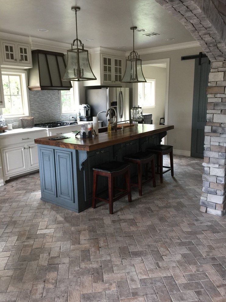 Example of a mid-sized transitional galley brick floor and gray floor enclosed kitchen design in Other with an undermount sink, raised-panel cabinets, white cabinets, wood countertops, gray backsplash, matchstick tile backsplash, stainless steel appliances, an island and white countertops