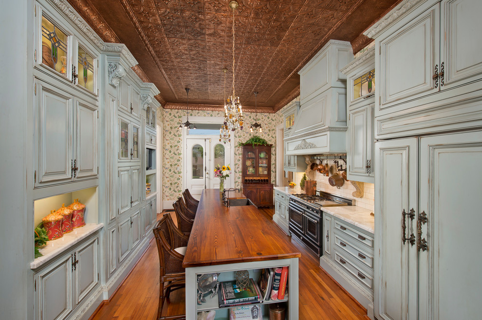 Klassisk inredning av ett kök, med en rustik diskho, luckor med upphöjd panel, blå skåp, träbänkskiva, vitt stänkskydd, stänkskydd i tunnelbanekakel, svarta vitvaror, mellanmörkt trägolv och en köksö
