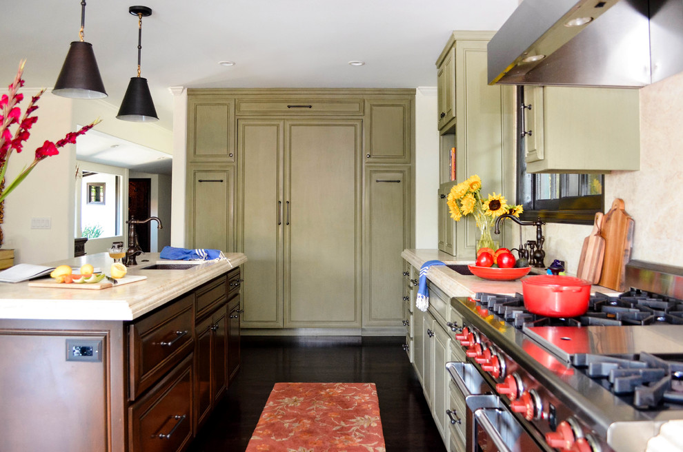 Eat-in kitchen - large mediterranean l-shaped dark wood floor and brown floor eat-in kitchen idea in Los Angeles with an undermount sink, raised-panel cabinets, green cabinets, quartzite countertops, beige backsplash, stone slab backsplash, paneled appliances, an island and beige countertops