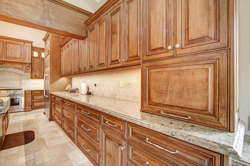 Example of a large classic l-shaped porcelain tile and white floor open concept kitchen design in Los Angeles with an undermount sink, raised-panel cabinets, medium tone wood cabinets, quartz countertops, beige backsplash, travertine backsplash, stainless steel appliances, an island and beige countertops