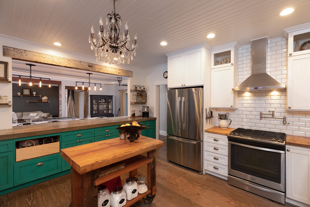 Elegant u-shaped medium tone wood floor, brown floor and shiplap ceiling kitchen photo in Portland with shaker cabinets, white cabinets, wood countertops, white backsplash, subway tile backsplash, stainless steel appliances, an island and brown countertops
