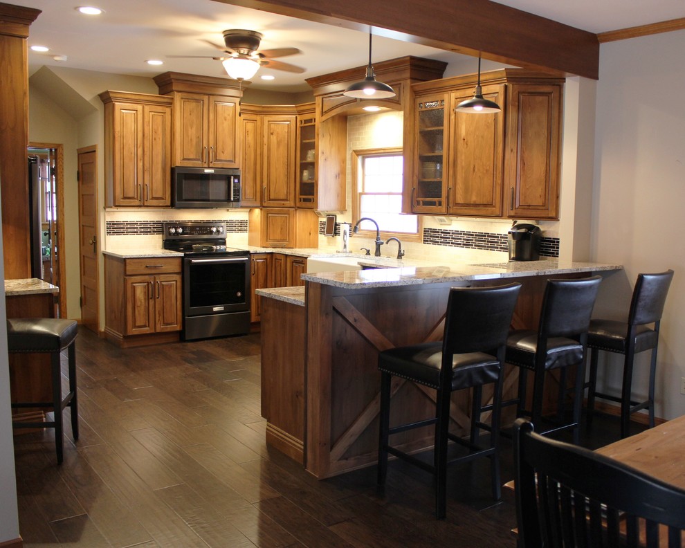 Example of a large mountain style u-shaped medium tone wood floor and brown floor eat-in kitchen design in Other with a farmhouse sink, raised-panel cabinets, medium tone wood cabinets, granite countertops, beige backsplash, travertine backsplash, black appliances, a peninsula and beige countertops