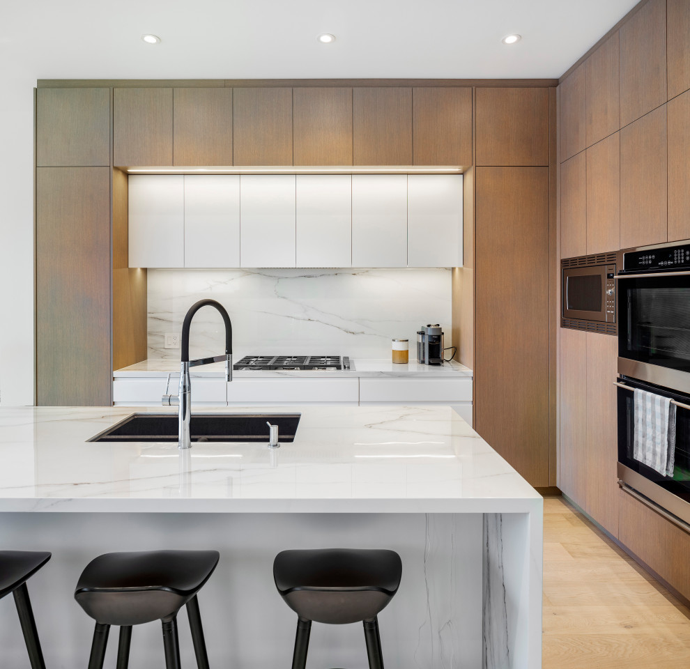 Inspiration for a mid-sized modern l-shaped light wood floor and white floor eat-in kitchen remodel in Toronto with an undermount sink, flat-panel cabinets, light wood cabinets, quartzite countertops, white backsplash, marble backsplash, black appliances, an island and white countertops