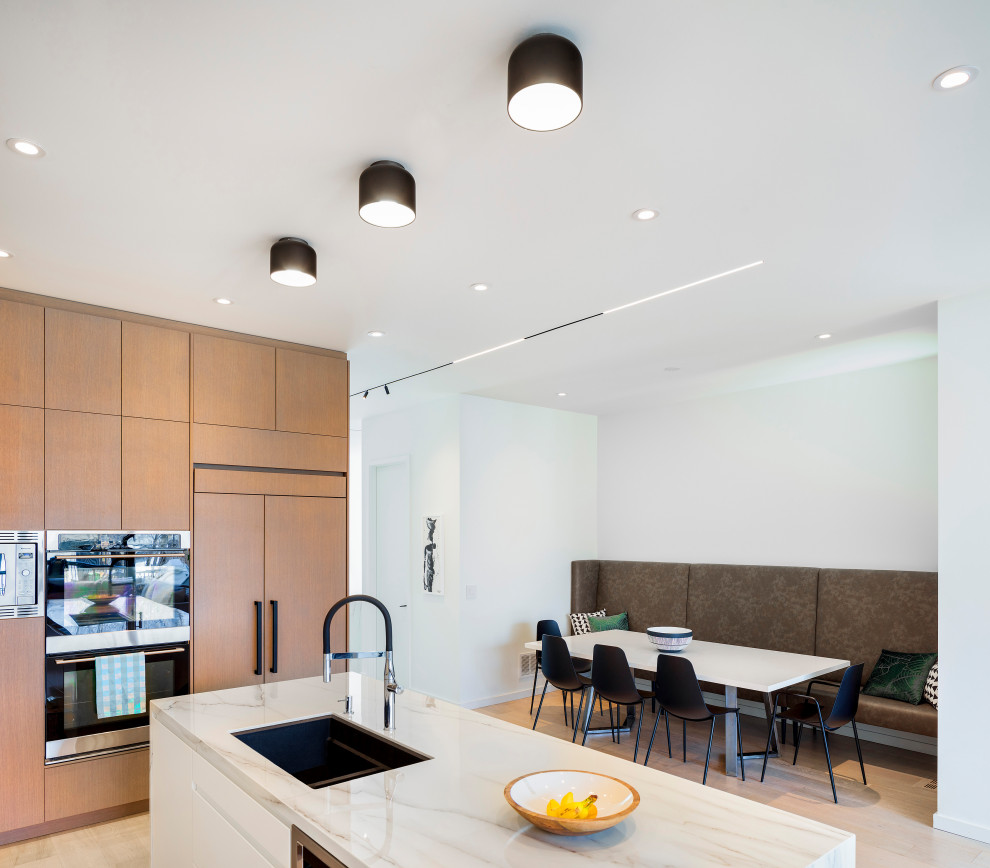 Eat-in kitchen - mid-sized modern l-shaped light wood floor and white floor eat-in kitchen idea in Toronto with an undermount sink, flat-panel cabinets, light wood cabinets, quartzite countertops, white backsplash, marble backsplash, black appliances, an island and white countertops