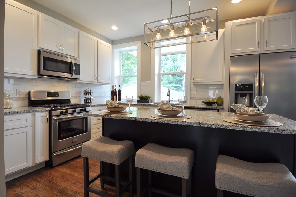 Mid-sized transitional l-shaped medium tone wood floor open concept kitchen photo in St Louis with an undermount sink, shaker cabinets, granite countertops, white backsplash, porcelain backsplash, stainless steel appliances and an island