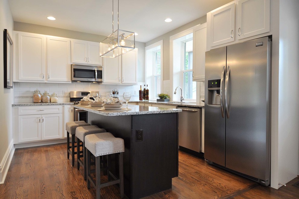 Open concept kitchen - mid-sized transitional l-shaped medium tone wood floor and brown floor open concept kitchen idea in St Louis with an undermount sink, shaker cabinets, granite countertops, white backsplash, porcelain backsplash, stainless steel appliances, an island and white cabinets