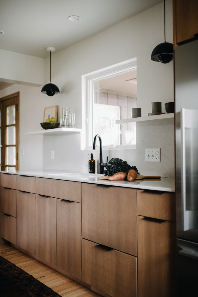 Photo of a scandinavian kitchen/diner in Minneapolis with a submerged sink, flat-panel cabinets, light wood cabinets, engineered stone countertops, white splashback, stainless steel appliances, light hardwood flooring, no island and white worktops.