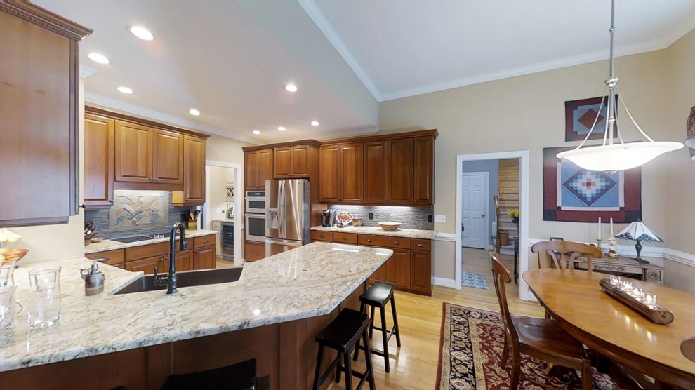 Large elegant l-shaped light wood floor and brown floor eat-in kitchen photo in Raleigh with a farmhouse sink, recessed-panel cabinets, medium tone wood cabinets, granite countertops, gray backsplash, slate backsplash, stainless steel appliances, a peninsula and beige countertops