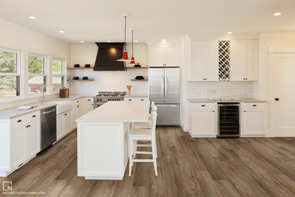 Huge vinyl floor and brown floor kitchen photo in Other with recessed-panel cabinets, white cabinets, white backsplash, subway tile backsplash, stainless steel appliances, an island and white countertops