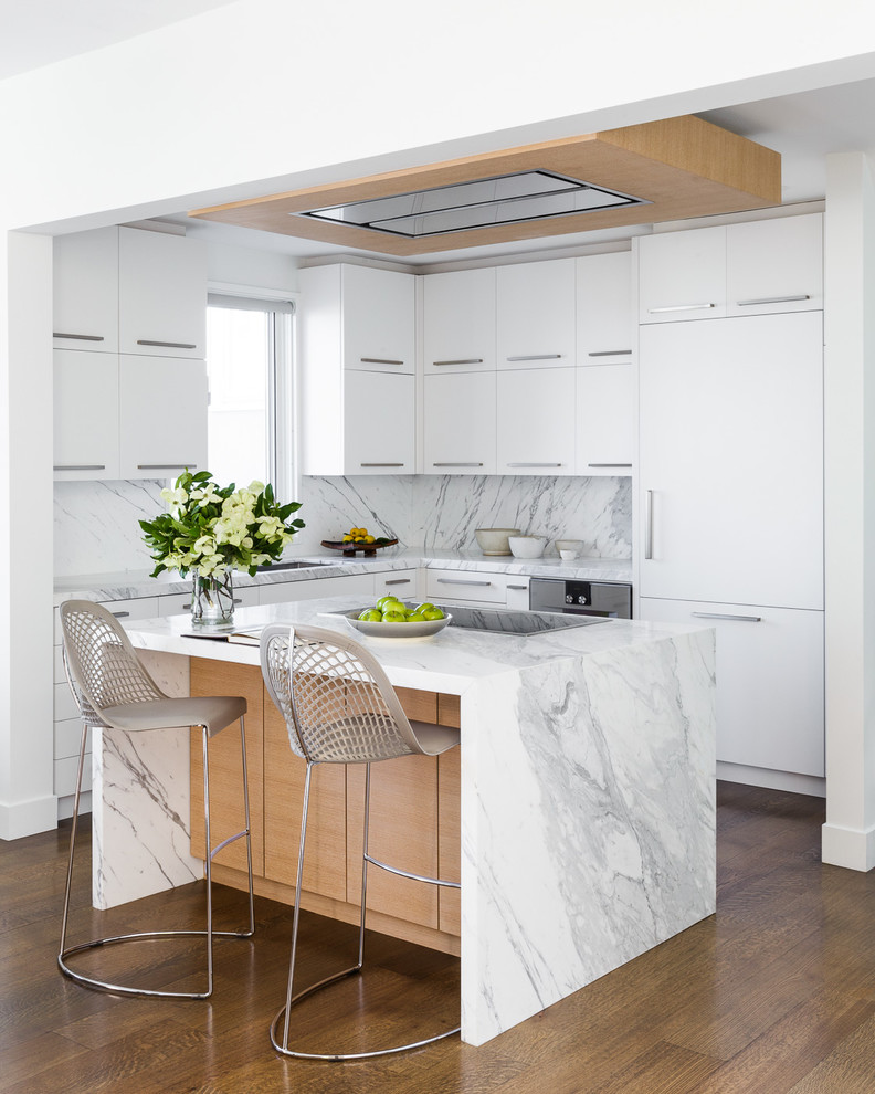 Example of a trendy l-shaped medium tone wood floor and brown floor kitchen design in San Francisco with an undermount sink, flat-panel cabinets, white cabinets, white backsplash, stone slab backsplash, paneled appliances, an island and white countertops