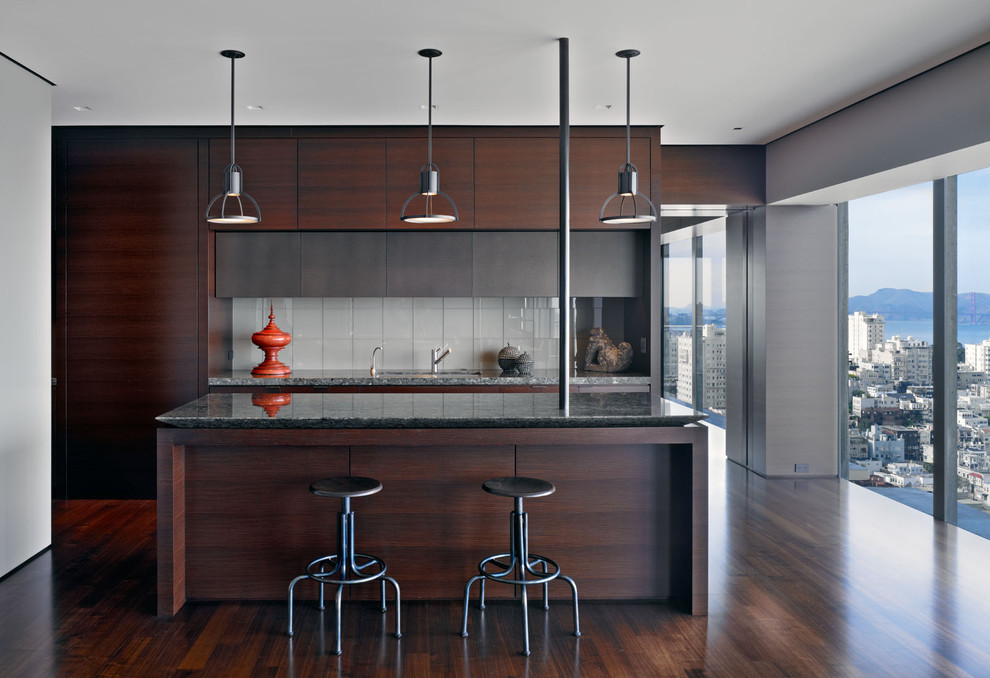 Cette photo montre une cuisine moderne en bois foncé avec un placard à porte plane, une crédence blanche, une crédence en carreau de verre, parquet foncé et un sol marron.