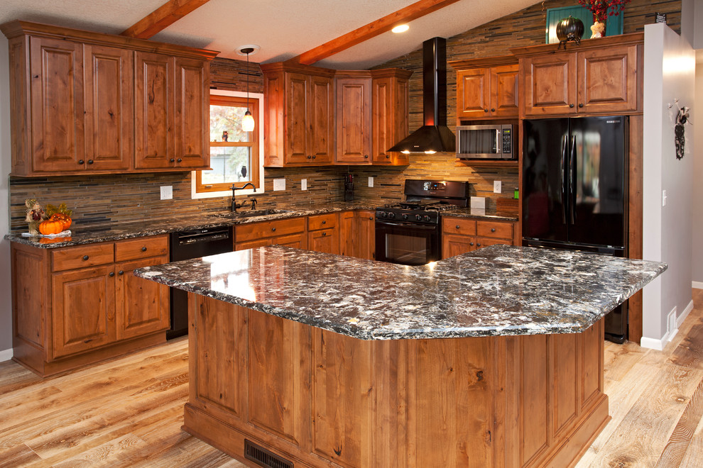 Inredning av ett rustikt mellanstort kök, med en undermonterad diskho, luckor med upphöjd panel, skåp i mellenmörkt trä, bänkskiva i kvarts, grönt stänkskydd, stänkskydd i stenkakel, svarta vitvaror, ljust trägolv och en köksö