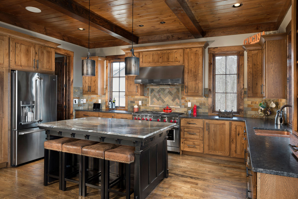 Rustic u-shaped kitchen in Other with a submerged sink, shaker cabinets, medium wood cabinets, brown splashback, stainless steel appliances, medium hardwood flooring, an island, brown floors and black worktops.