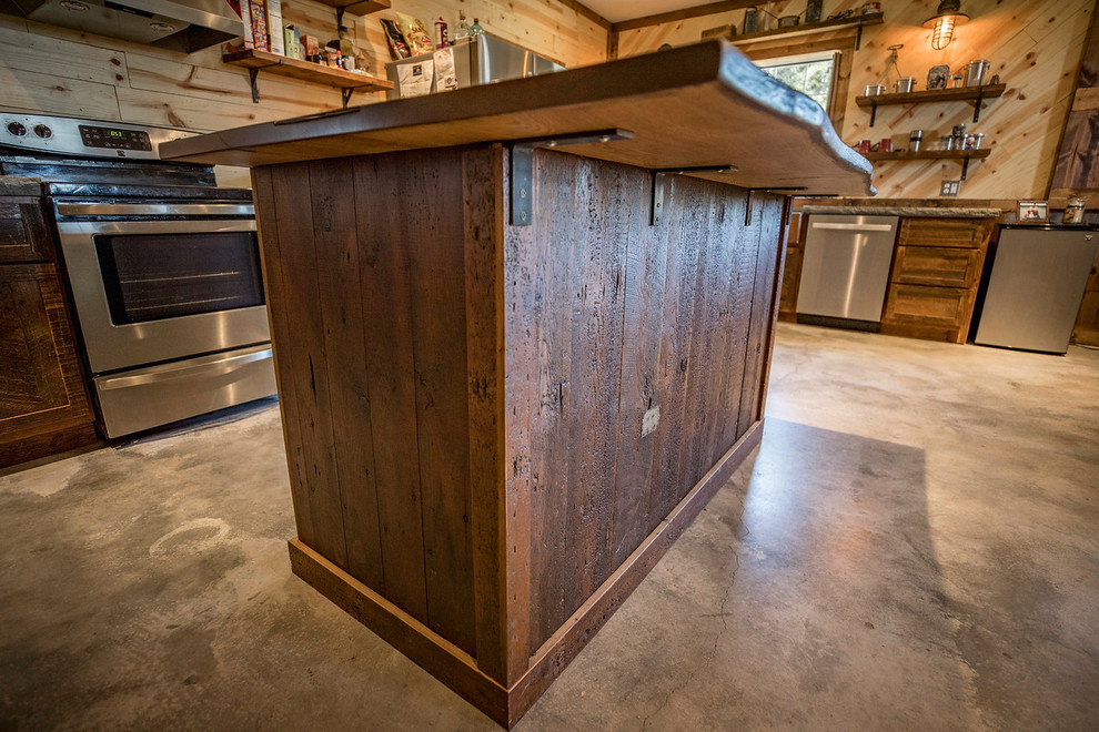 Photo of a small rustic u-shaped kitchen/diner in Wichita with a belfast sink, shaker cabinets, distressed cabinets, concrete worktops, brown splashback, wood splashback, stainless steel appliances, concrete flooring, an island and grey floors.