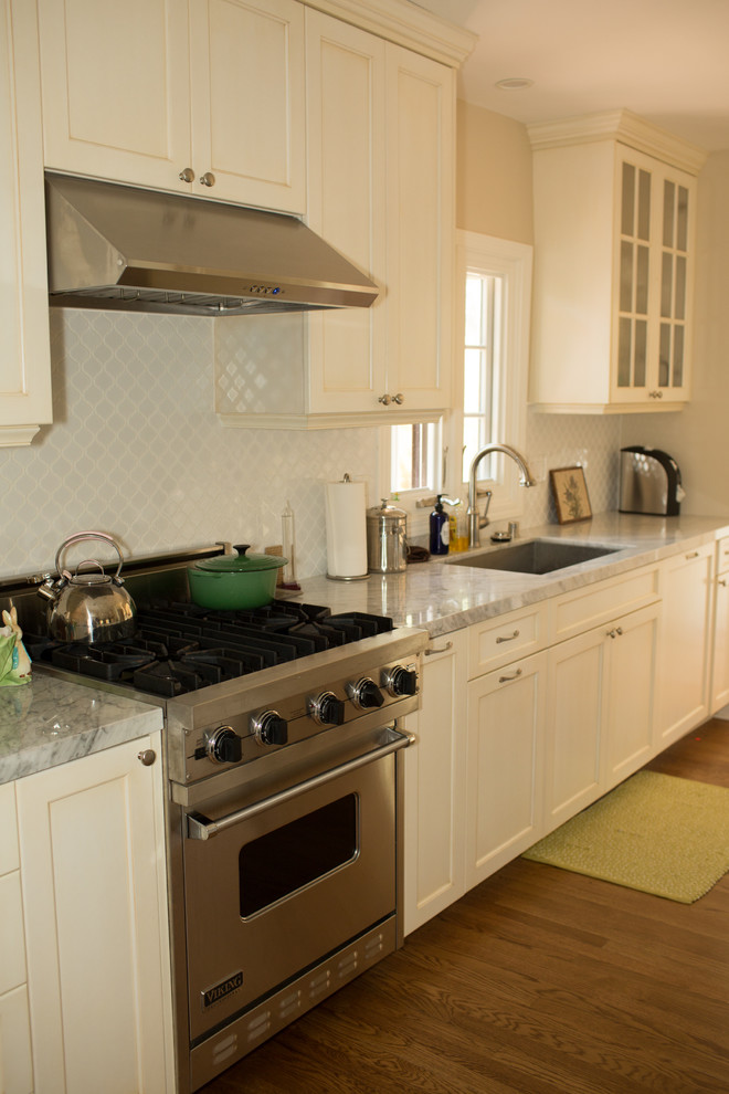 Klassisk inredning av ett mellanstort kök, med en nedsänkt diskho, luckor med upphöjd panel, vita skåp, marmorbänkskiva, grått stänkskydd, stänkskydd i mosaik, rostfria vitvaror, mellanmörkt trägolv och en halv köksö