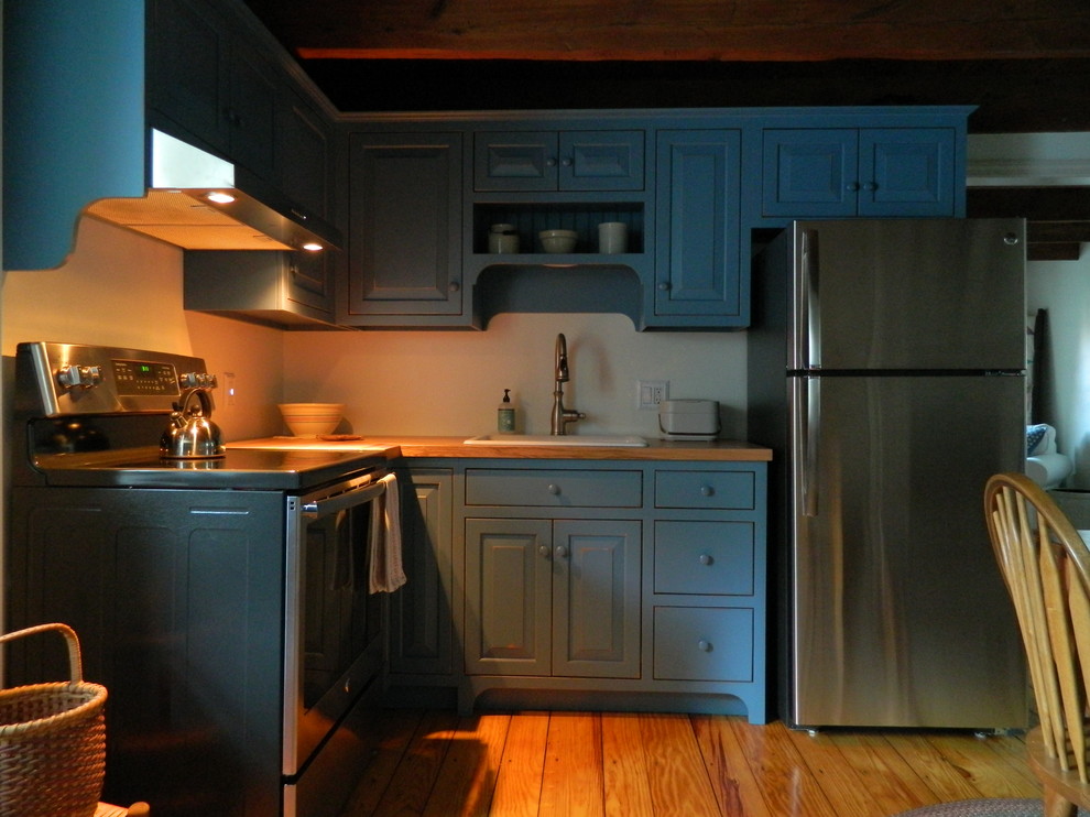 Idée de décoration pour une petite cuisine américaine chalet en L avec des portes de placard bleues et un plan de travail en bois.