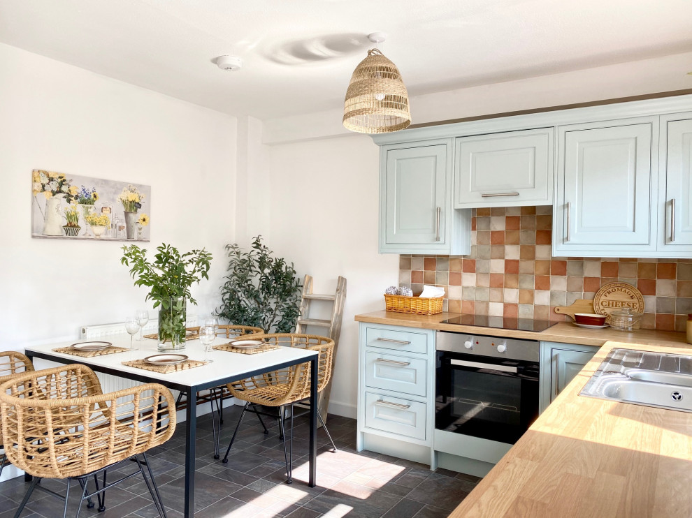Bild på ett mellanstort lantligt beige beige kök, med en nedsänkt diskho, skåp i shakerstil, blå skåp, träbänkskiva, flerfärgad stänkskydd, stänkskydd i keramik, rostfria vitvaror, linoleumgolv och grått golv