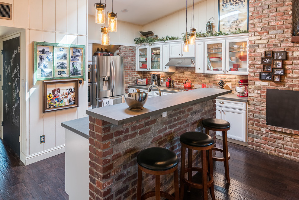 Design ideas for a medium sized rustic l-shaped open plan kitchen in Sacramento with glass-front cabinets, white cabinets, concrete worktops, brown splashback, brick splashback, stainless steel appliances, dark hardwood flooring, an island, brown floors and grey worktops.