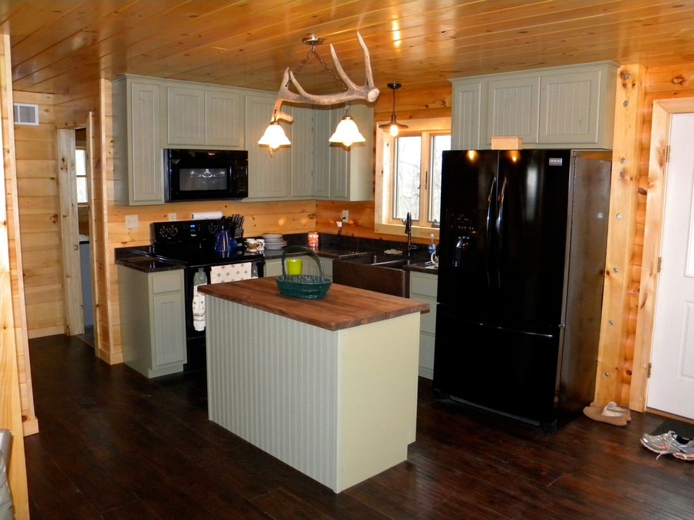 Modelo de cocina rural con fregadero sobremueble, puertas de armario verdes, encimera de madera y electrodomésticos negros