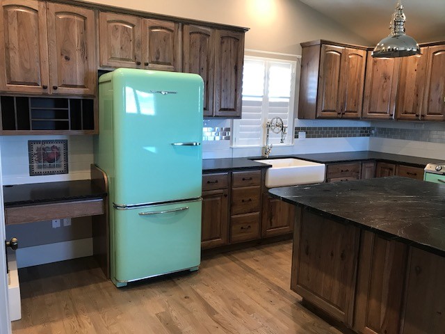 Example of a large arts and crafts l-shaped medium tone wood floor and brown floor kitchen design in Boise with a farmhouse sink, raised-panel cabinets, medium tone wood cabinets, soapstone countertops, white backsplash, subway tile backsplash, colored appliances and an island