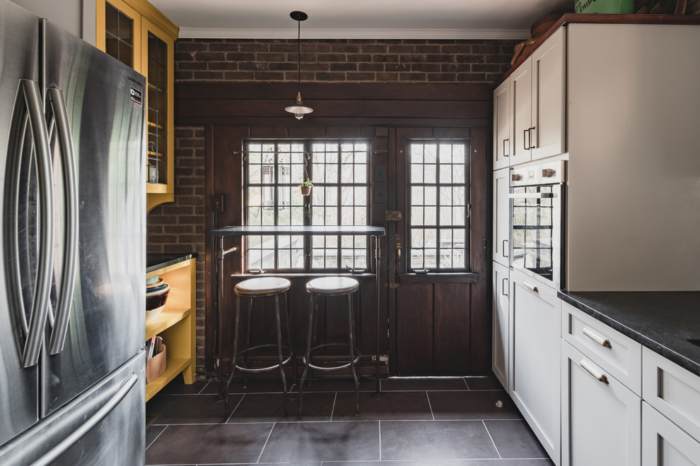 Foto på ett avskilt, litet rustikt svart l-kök, med en dubbel diskho, skåp i shakerstil, grå skåp, bänkskiva i täljsten, vitt stänkskydd, stänkskydd i terrakottakakel, rostfria vitvaror, skiffergolv och lila golv