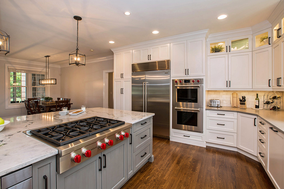 Example of a mid-sized cottage chic l-shaped medium tone wood floor and brown floor enclosed kitchen design in Cincinnati with an undermount sink, shaker cabinets, white cabinets, quartz countertops, gray backsplash, stone tile backsplash, stainless steel appliances and an island