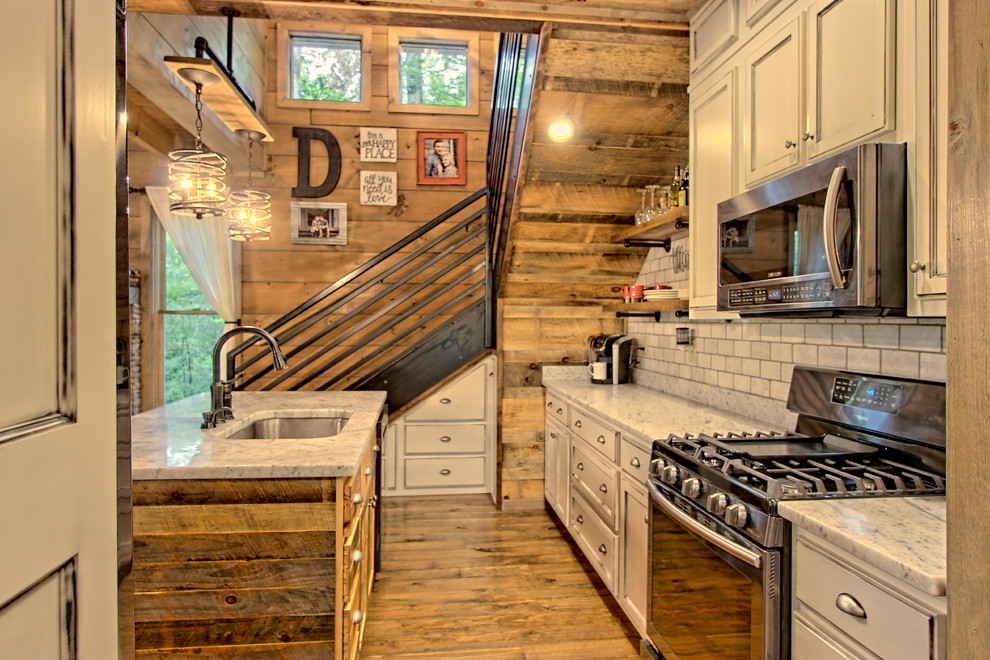 Foto på ett litet rustikt kök med öppen planlösning, med en nedsänkt diskho, luckor med infälld panel, skåp i slitet trä, granitbänkskiva, vitt stänkskydd, stänkskydd i stenkakel, rostfria vitvaror, målat trägolv, en köksö och brunt golv