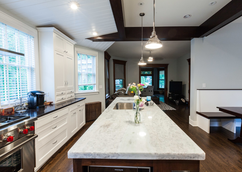 Eklektisk inredning av ett stort kök, med en undermonterad diskho, luckor med infälld panel, vita skåp, bänkskiva i kvartsit, rostfria vitvaror, mellanmörkt trägolv och en köksö