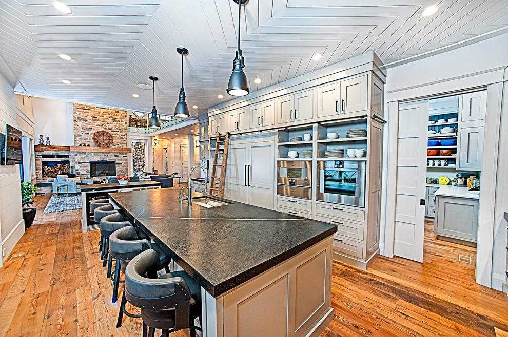 Exempel på ett stort rustikt kök, med en undermonterad diskho, skåp i shakerstil, grå skåp, bänkskiva i täljsten, svart stänkskydd, stänkskydd i sten, rostfria vitvaror, mellanmörkt trägolv, flera köksöar och brunt golv