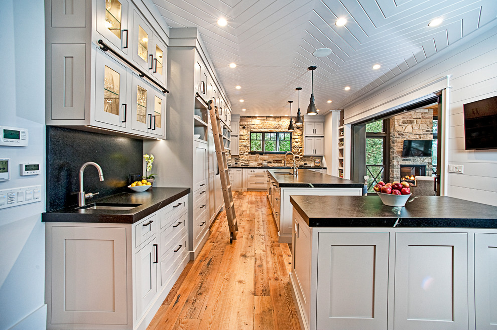 Exempel på ett stort rustikt kök, med en undermonterad diskho, skåp i shakerstil, grå skåp, bänkskiva i täljsten, svart stänkskydd, stänkskydd i sten, rostfria vitvaror, mellanmörkt trägolv, flera köksöar och brunt golv