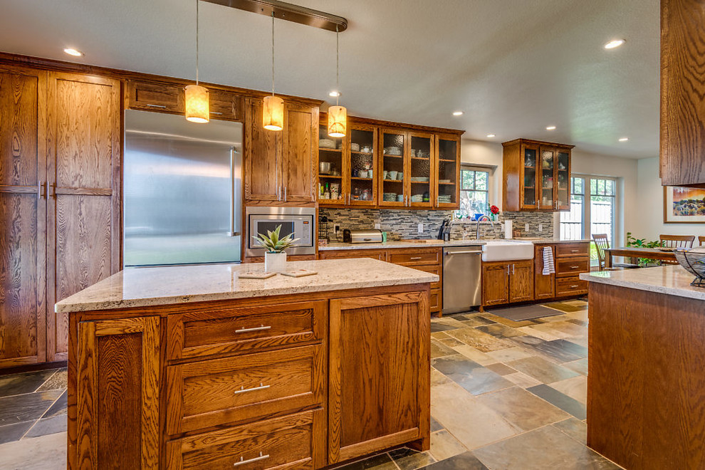 Huge country galley slate floor and multicolored floor eat-in kitchen photo in Dallas with a farmhouse sink, shaker cabinets, brown cabinets, granite countertops, multicolored backsplash, glass tile backsplash, stainless steel appliances, an island and multicolored countertops