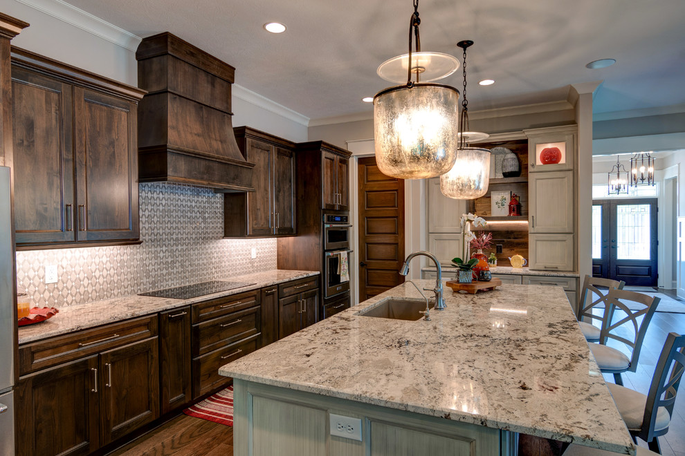 Photo of a medium sized rustic l-shaped kitchen in Indianapolis with a built-in sink, shaker cabinets, brown cabinets, granite worktops, grey splashback, cement tile splashback, stainless steel appliances, vinyl flooring, an island and brown floors.