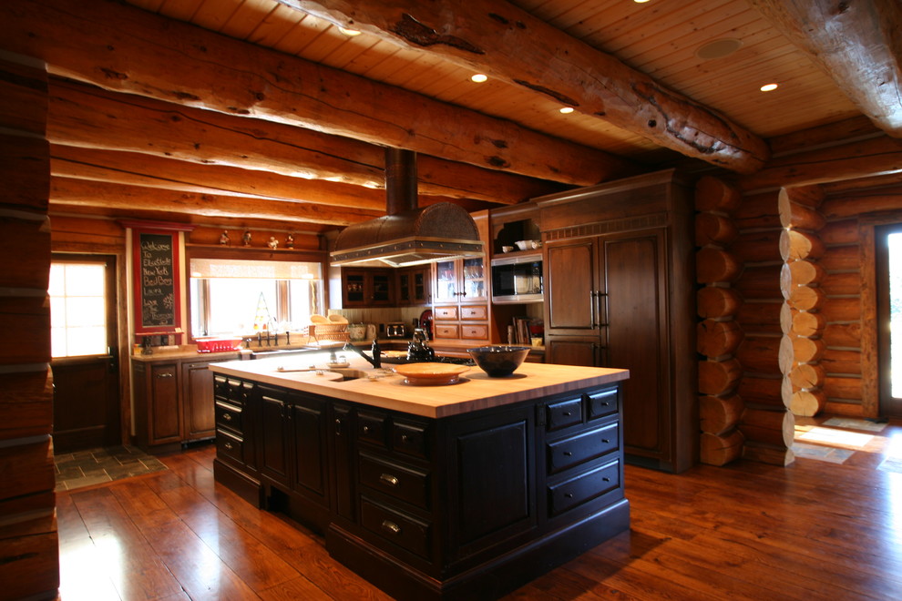 Cette image montre une très grande cuisine américaine encastrable chalet en L et bois brun avec un évier de ferme, un placard avec porte à panneau surélevé, un plan de travail en bois, un sol en bois brun et îlot.