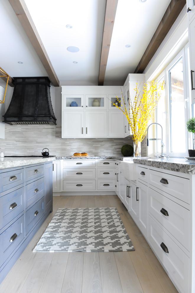 Bild på ett stort lantligt kök, med grått stänkskydd, stänkskydd i stenkakel, rostfria vitvaror, ljust trägolv, en köksö, skåp i shakerstil, blå skåp, brunt golv och en rustik diskho