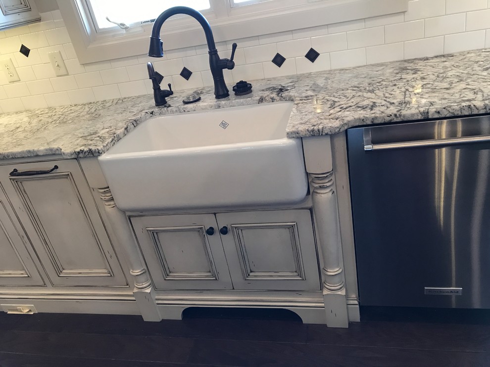 Example of a large country u-shaped dark wood floor and brown floor kitchen pantry design in Other with a farmhouse sink, beaded inset cabinets, distressed cabinets, granite countertops, white backsplash, porcelain backsplash, stainless steel appliances and an island