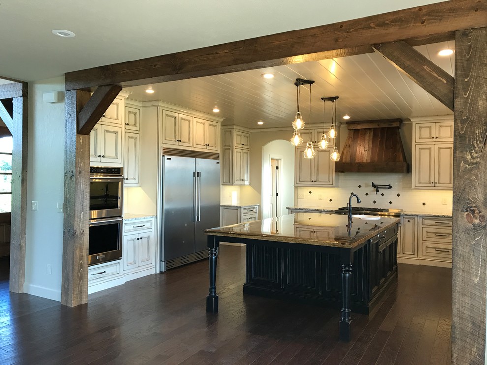 Example of a large cottage u-shaped dark wood floor and brown floor kitchen pantry design in Other with a farmhouse sink, beaded inset cabinets, distressed cabinets, granite countertops, white backsplash, porcelain backsplash, stainless steel appliances and an island