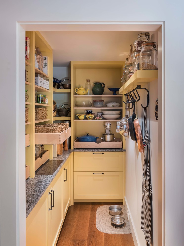 Photo of a medium sized farmhouse l-shaped kitchen pantry in Boston with a submerged sink, shaker cabinets, yellow cabinets, wood worktops, brown splashback, stone tiled splashback, stainless steel appliances, medium hardwood flooring, an island and brown floors.