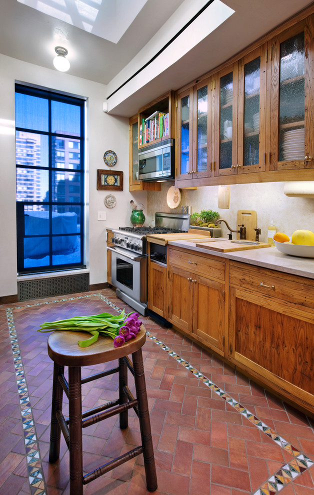 Example of a mid-sized farmhouse galley brick floor and red floor enclosed kitchen design in New York with an undermount sink, shaker cabinets, medium tone wood cabinets, limestone countertops, beige backsplash, stone slab backsplash, stainless steel appliances and no island