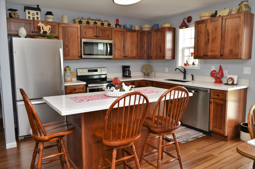 Inspiration for a medium sized rustic l-shaped open plan kitchen in Chicago with a submerged sink, shaker cabinets, medium wood cabinets, composite countertops, stainless steel appliances, medium hardwood flooring, an island, brown floors and white worktops.