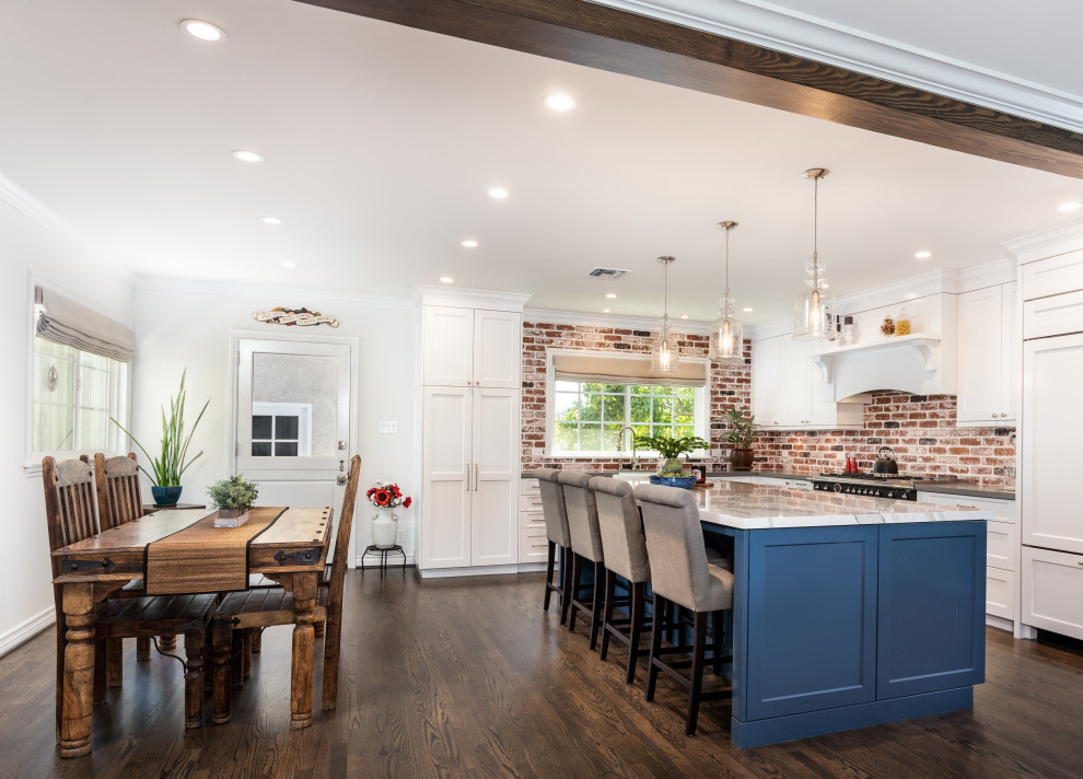 Inspiration for a mid-sized cottage l-shaped dark wood floor, brown floor and exposed beam open concept kitchen remodel in Los Angeles with a farmhouse sink, shaker cabinets, white cabinets, quartz countertops, multicolored backsplash, brick backsplash, black appliances, an island and gray countertops