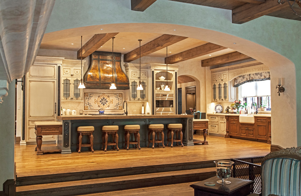 Klassisk inredning av ett stort beige beige kök, med luckor med upphöjd panel, en köksö, en rustik diskho, beige skåp, beige stänkskydd, integrerade vitvaror, mellanmörkt trägolv och brunt golv