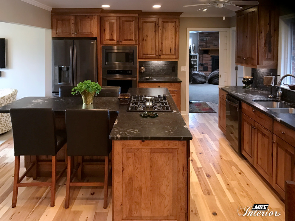 Inredning av ett rustikt stort kök, med en undermonterad diskho, luckor med upphöjd panel, skåp i mellenmörkt trä, granitbänkskiva, grått stänkskydd, stänkskydd i keramik, rostfria vitvaror, ljust trägolv, en köksö och beiget golv