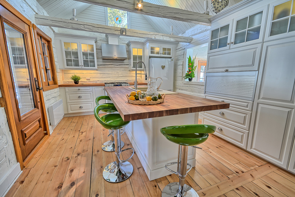 Bild på ett avskilt, litet rustikt u-kök, med en rustik diskho, luckor med upphöjd panel, vita skåp, träbänkskiva, vitt stänkskydd, stänkskydd i trä, integrerade vitvaror, ljust trägolv och en köksö