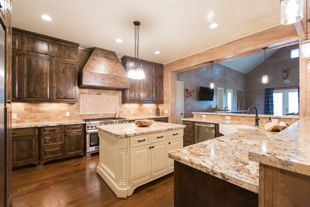 This is an example of a large rustic u-shaped open plan kitchen in Houston with a belfast sink, raised-panel cabinets, dark wood cabinets, granite worktops, beige splashback, ceramic splashback, stainless steel appliances, medium hardwood flooring, an island and brown floors.