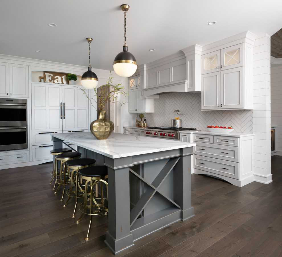 Photo of a traditional kitchen in Other with recessed-panel cabinets, white cabinets, white splashback, stainless steel appliances, dark hardwood flooring, an island, brown floors and white worktops.