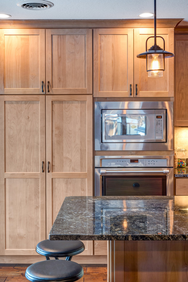 Example of a mid-sized classic l-shaped medium tone wood floor eat-in kitchen design in Minneapolis with an undermount sink, shaker cabinets, medium tone wood cabinets, granite countertops, beige backsplash, stone tile backsplash, stainless steel appliances and an island
