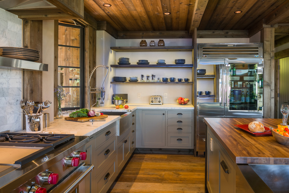 Example of a mid-sized mountain style l-shaped medium tone wood floor kitchen design in San Francisco with a farmhouse sink, gray cabinets, white backsplash, stainless steel appliances, an island and marble countertops