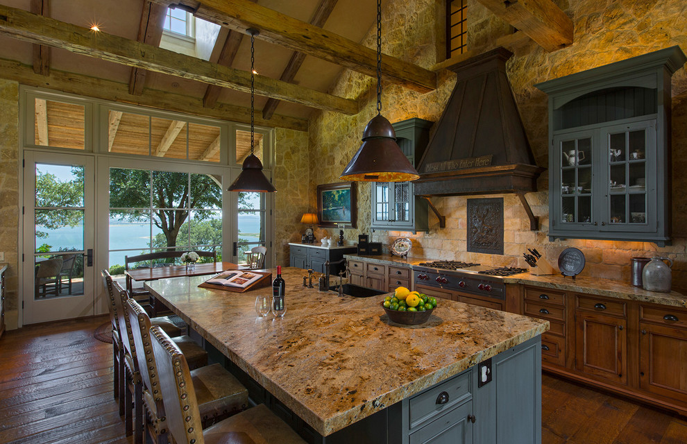 Example of a mid-sized mountain style l-shaped concrete floor eat-in kitchen design in Austin with a drop-in sink, recessed-panel cabinets, medium tone wood cabinets, granite countertops, beige backsplash, stone tile backsplash, stainless steel appliances and an island